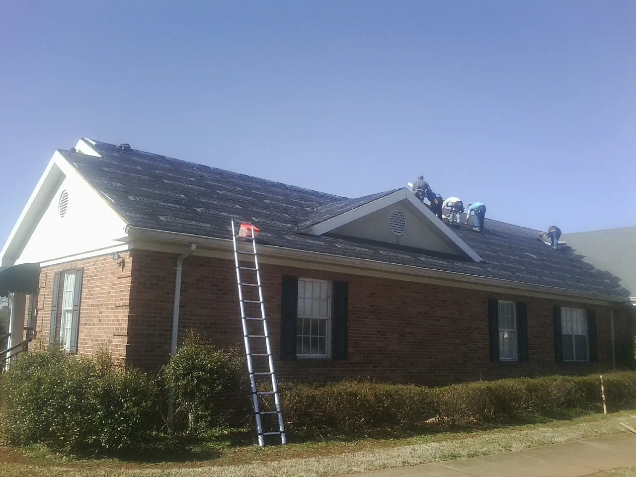 Crew tearing shingles off a brick ranch roof with a ladder set — Metal Roof Repair work by our crew in Clarks Summit