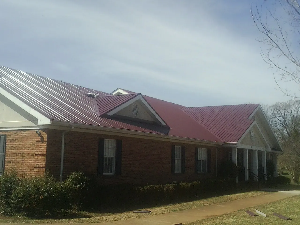 Red metal roof with gabled entries on a long brick building, from a Hail Damage Roof Repair job in Clarks Summit