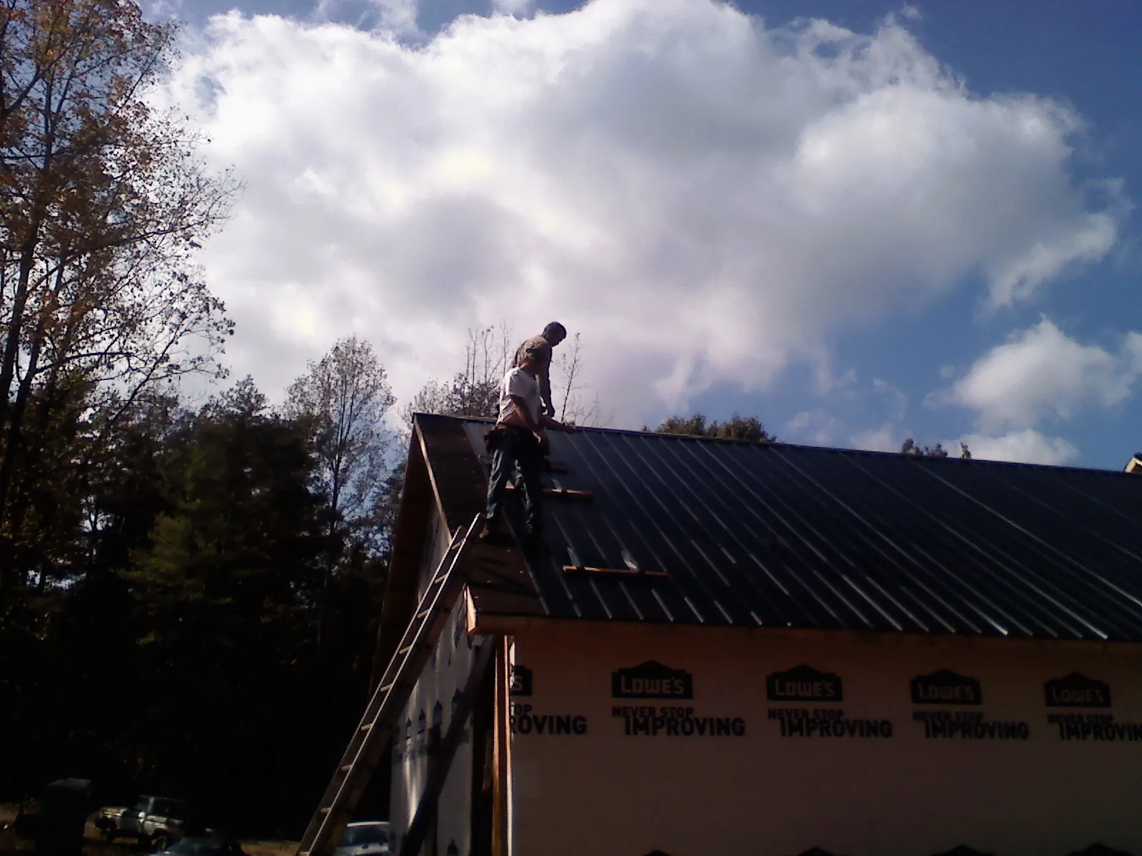Roofer fastening dark metal panels high against a cloudy sky, from a Roof Inspection job in Clarks Summit