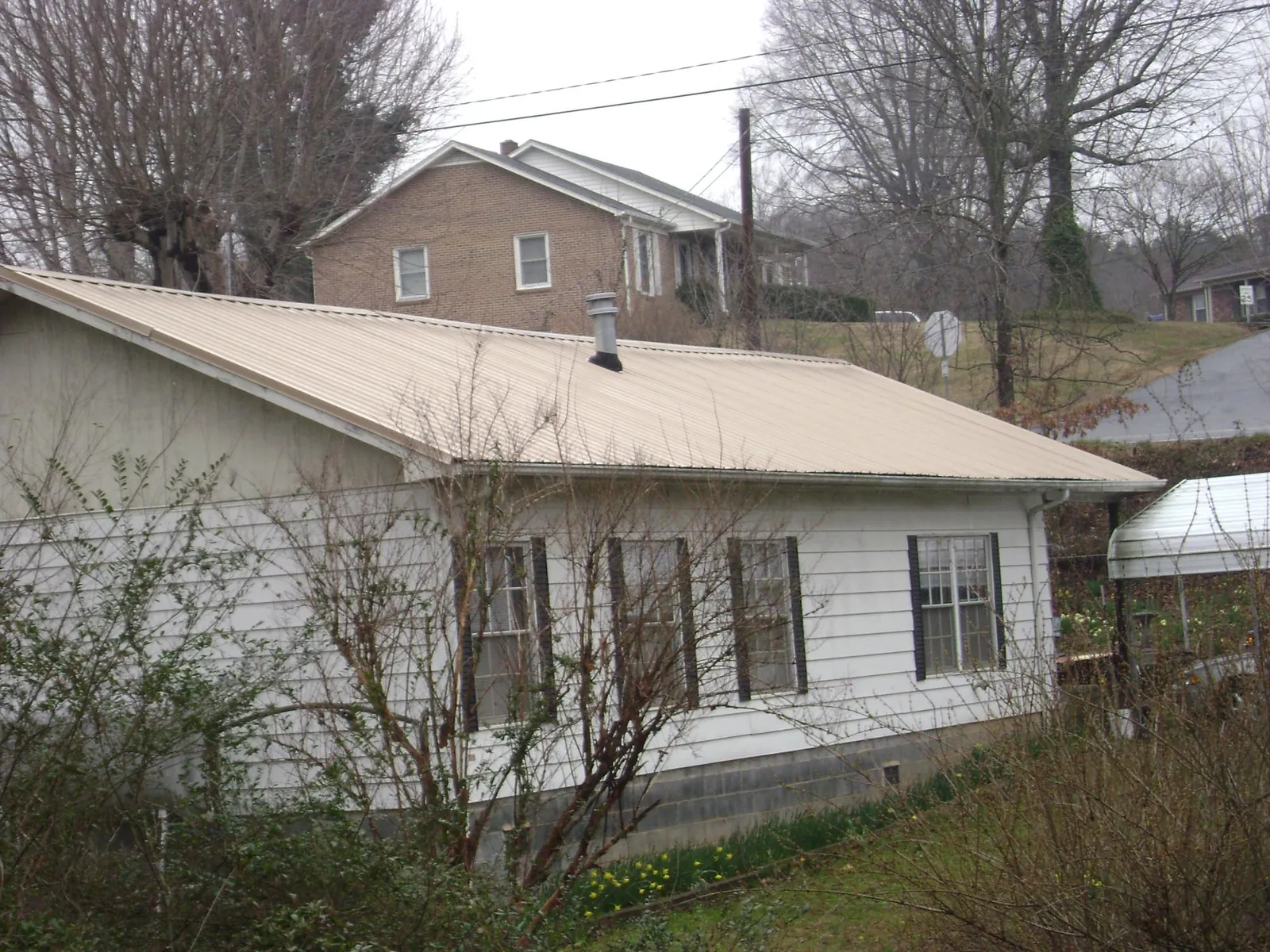 Tan metal roof on a white sided house set into a hillside — Commercial Roofing by Roofing Brothers in Clarks Summit